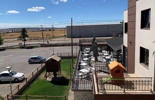 Un patio con mobiliario exterior, una casita de juegos y un estacionamiento cercado.