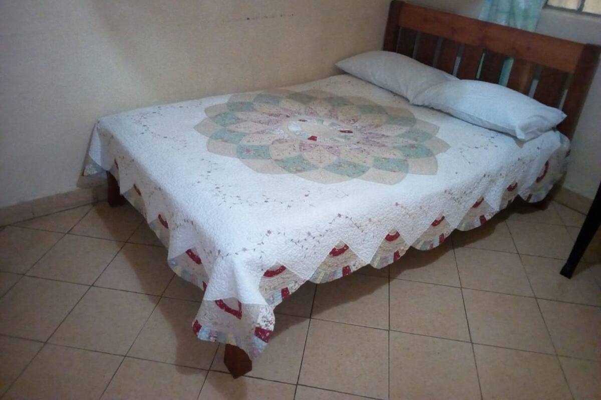 A bed with a quilt, a wooden headboard, and a tiled floor.