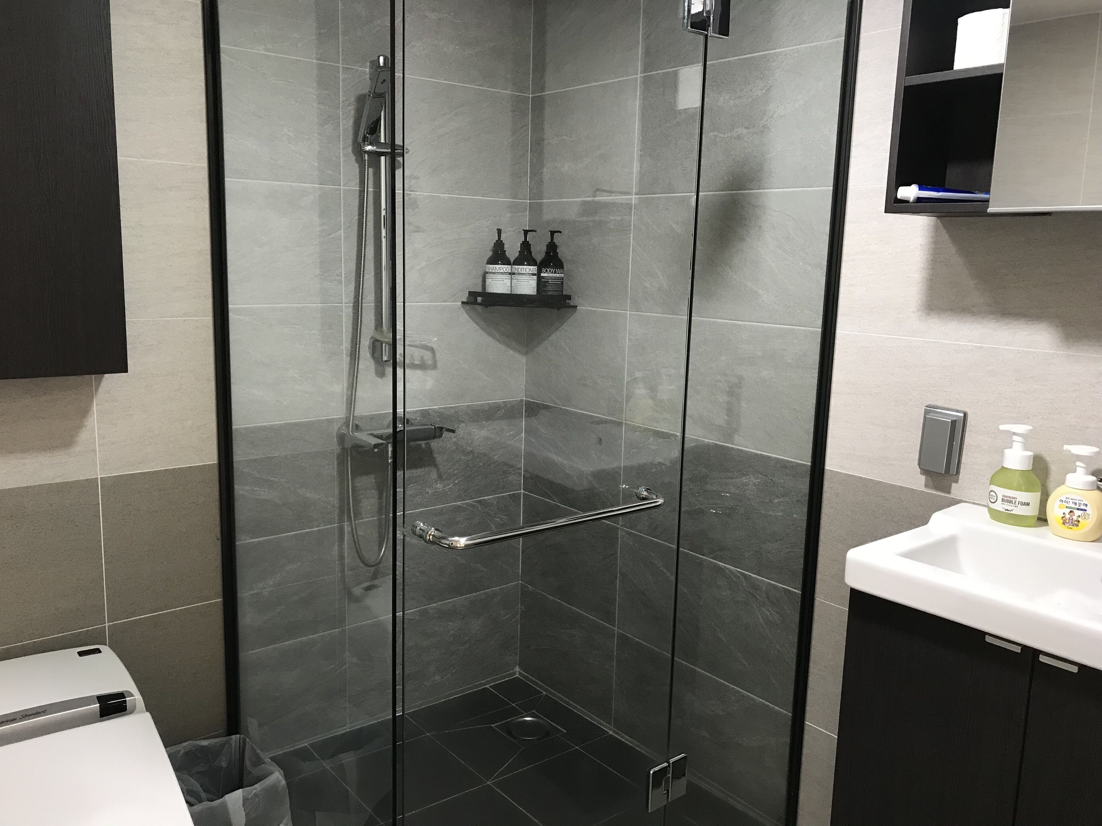 A modern bathroom with a glass-enclosed shower, a white sink, and toiletries on the countertop.