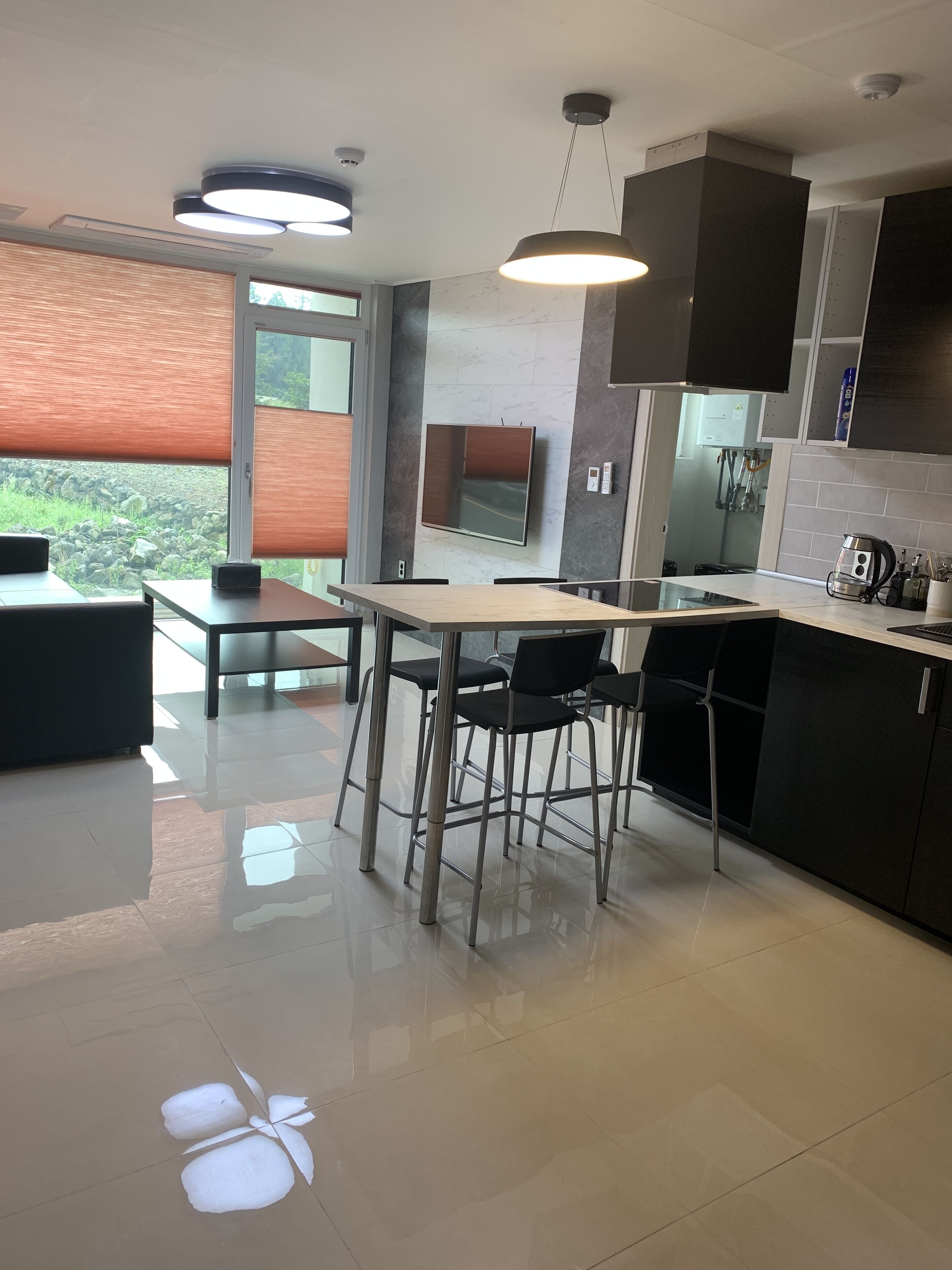A modern kitchen with a dining area, featuring a large island, black chairs, and a flat-screen TV mounted on the wall.