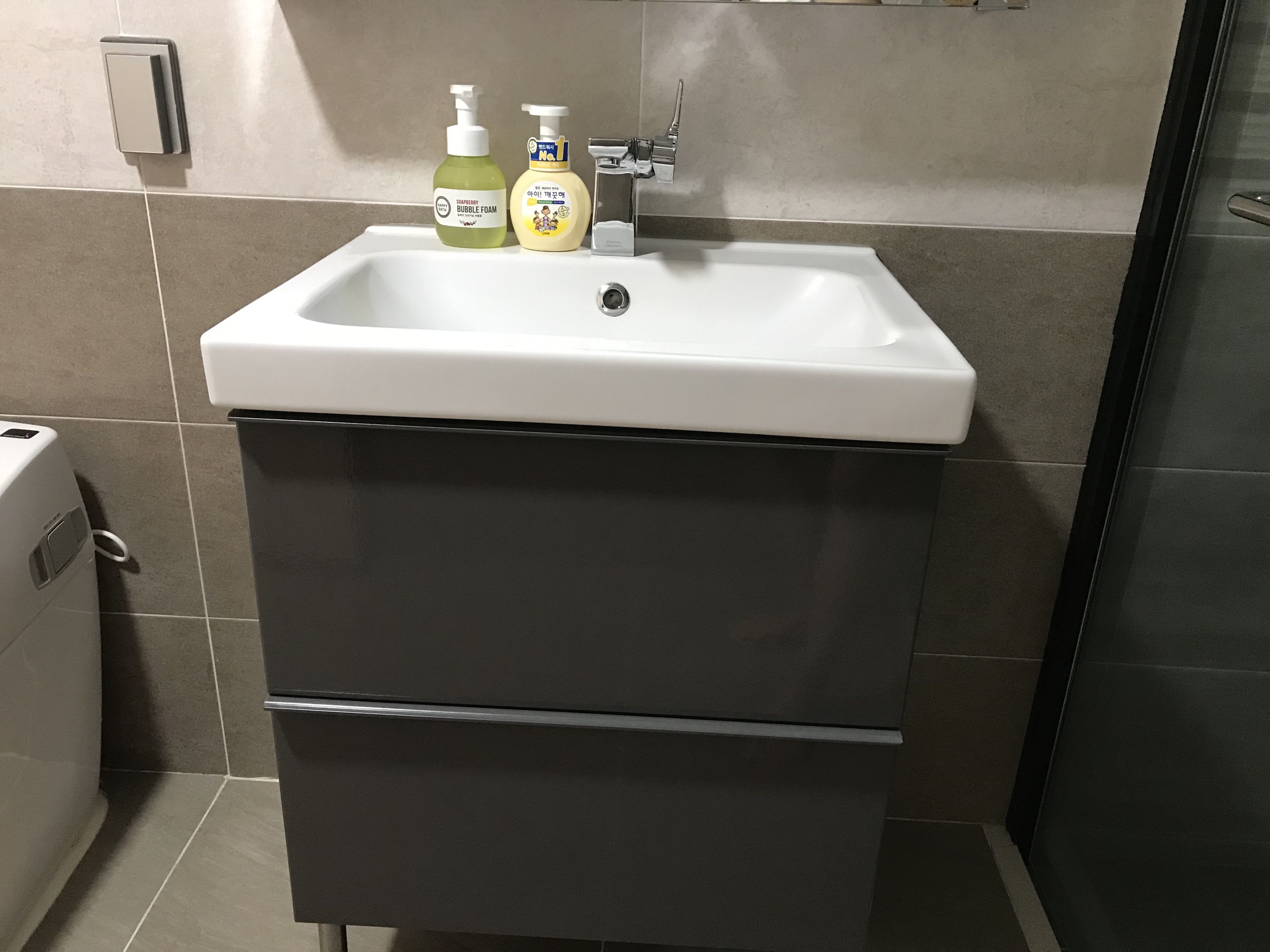 A bathroom with a white sink, two bottles of soap, and a toilet.