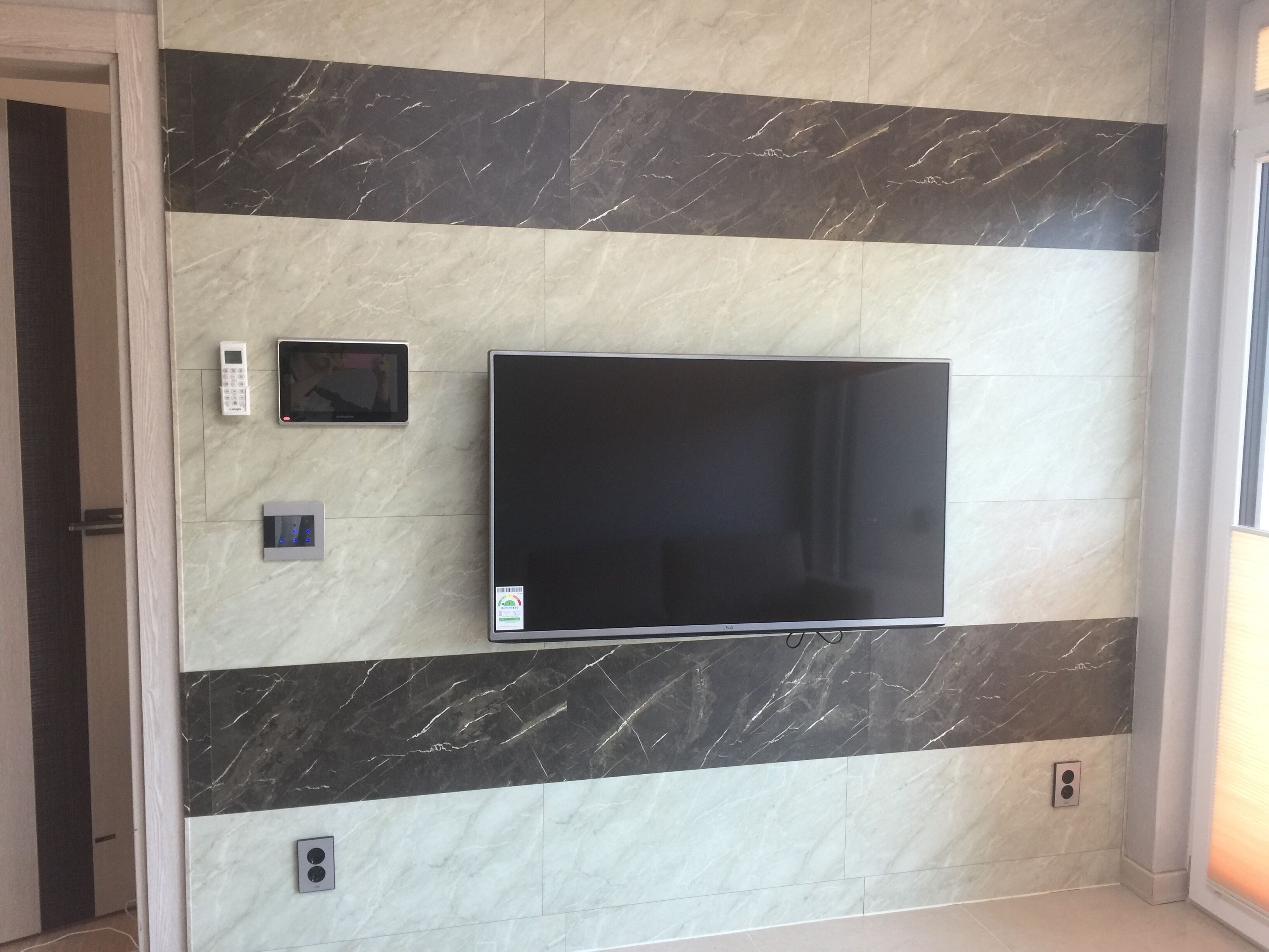 A wall-mounted flat-screen TV in a room with a tiled floor and a door to the left.