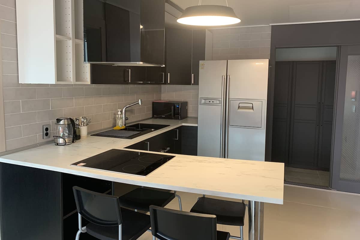 A modern kitchen with a white countertop, black chairs, a stainless steel refrigerator, and a built-in oven.
