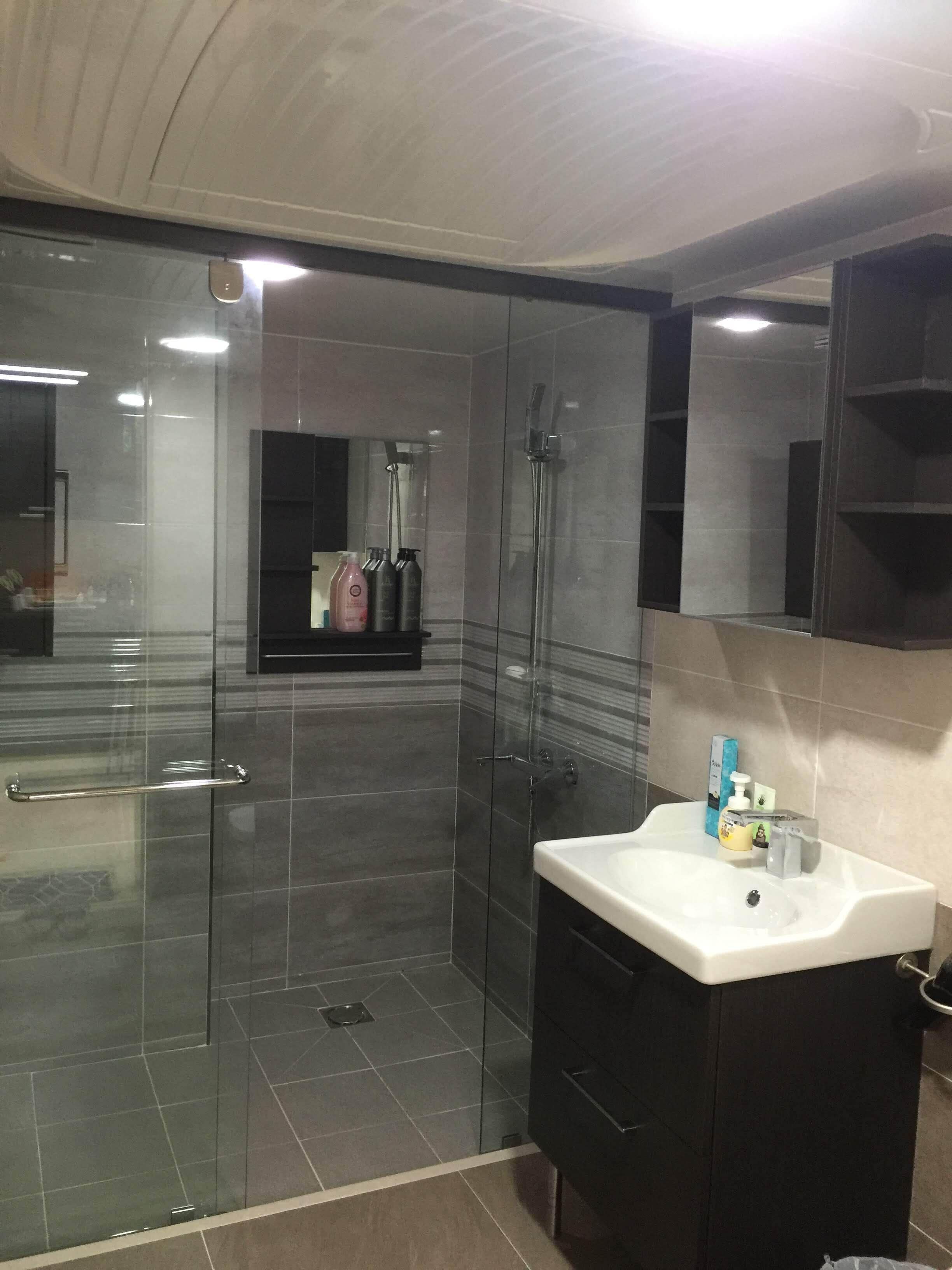 Un baño moderno con ducha acristalada, lavamanos blanco y mueble oscuro.