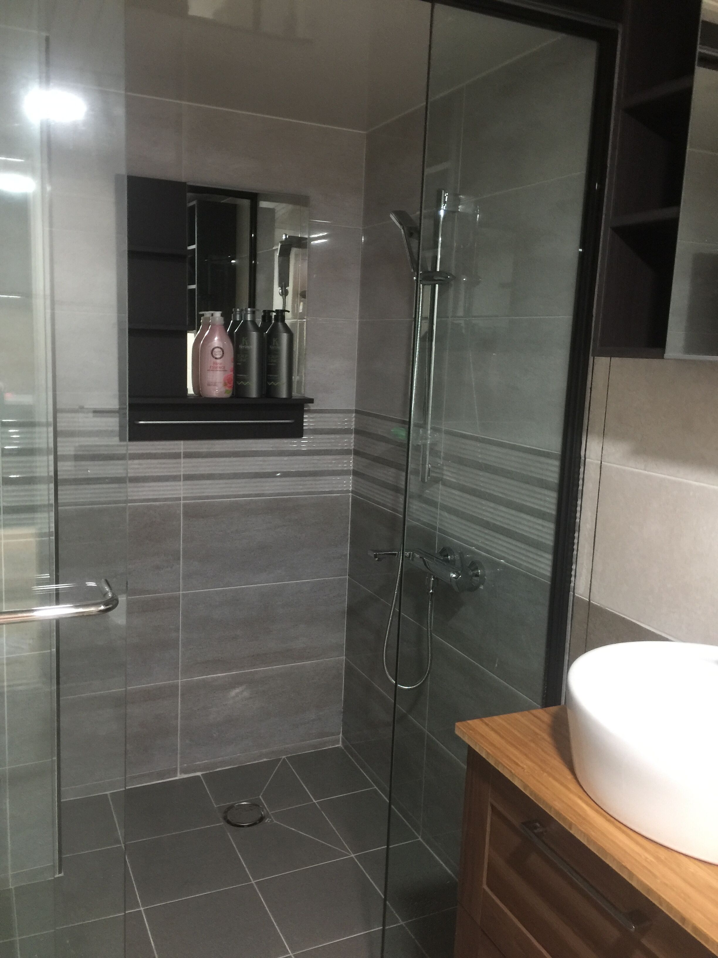 Une salle de bain moderne avec une douche à parois de verre, un meuble-lavabo avec un plan de travail en bois et un miroir au-dessus du lavabo.