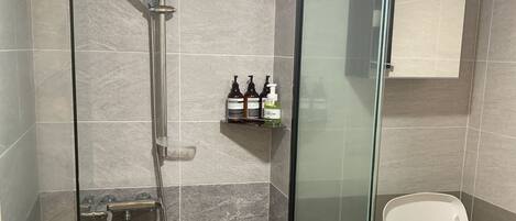 A modern bathroom with a glass-enclosed shower, a toilet, and a shelf with toiletries.