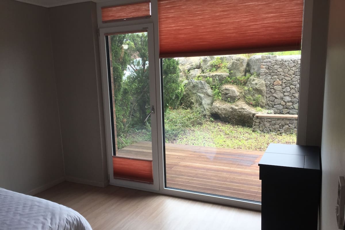 A room with a bed, a sliding glass door leading to an outdoor area with a wooden deck and a stone wall.