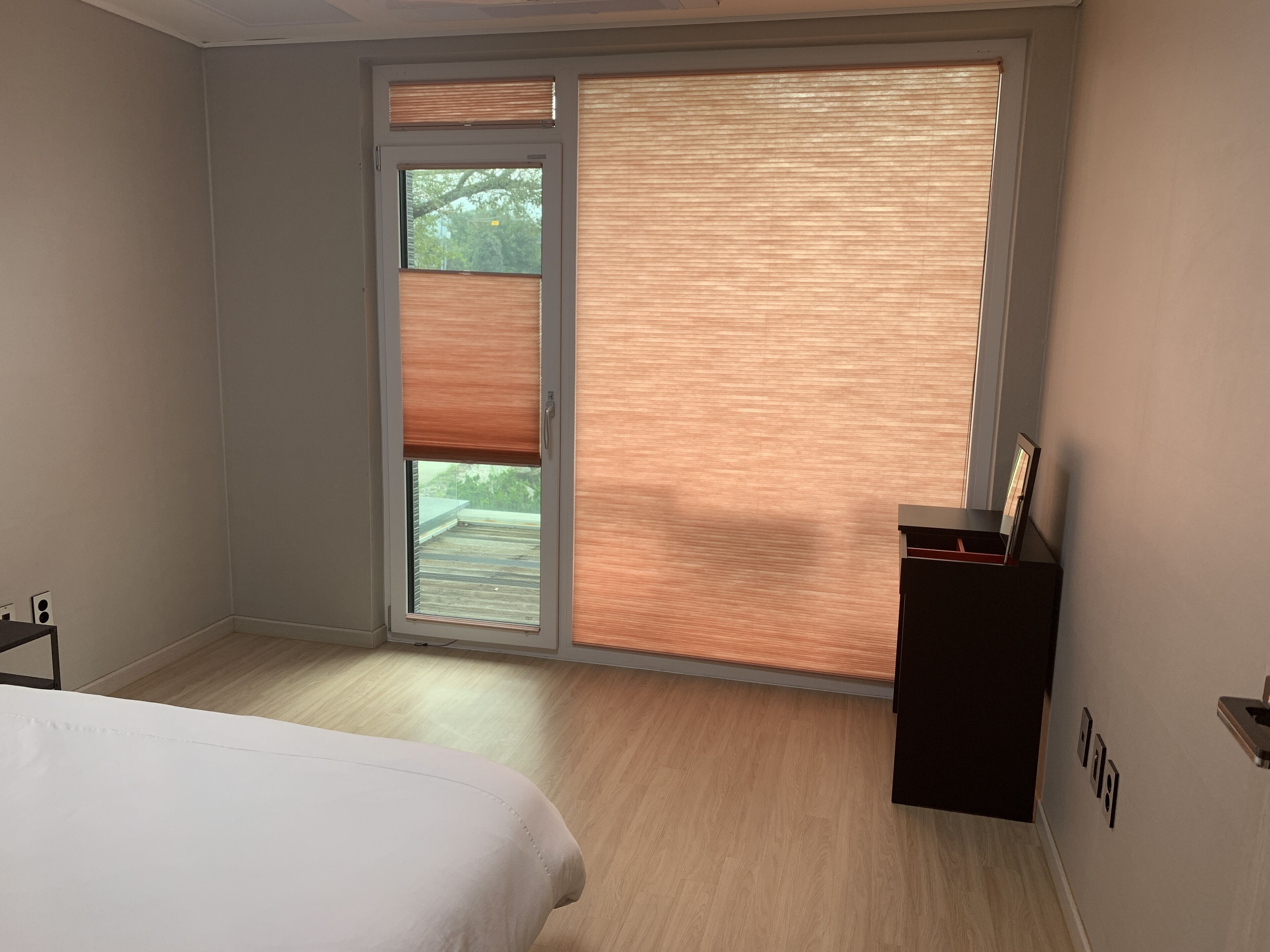 A bedroom with a bed, a desk, and a sliding glass door to a balcony.