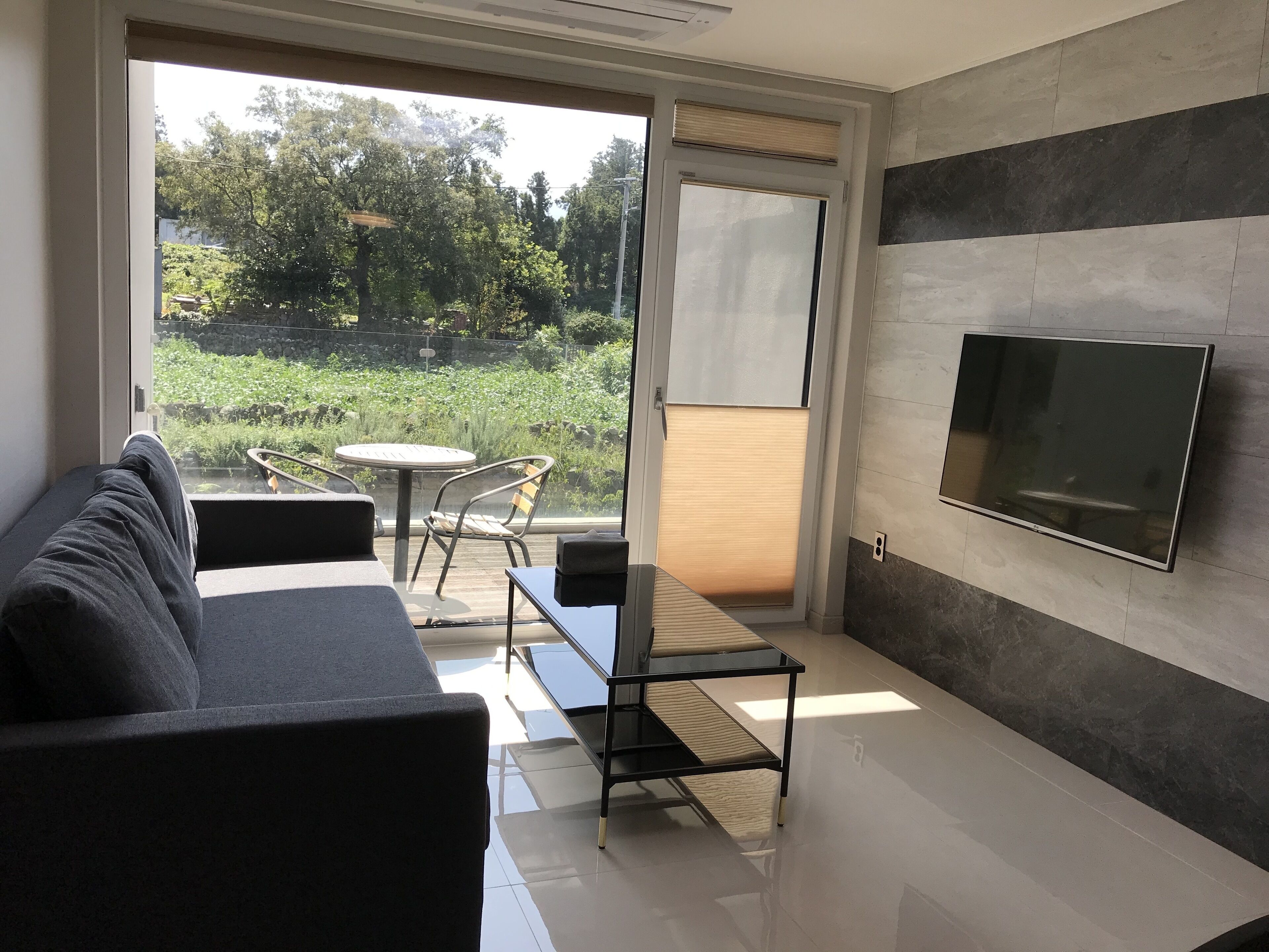A modern living room with a sofa, a glass table, and a TV mounted on the wall.