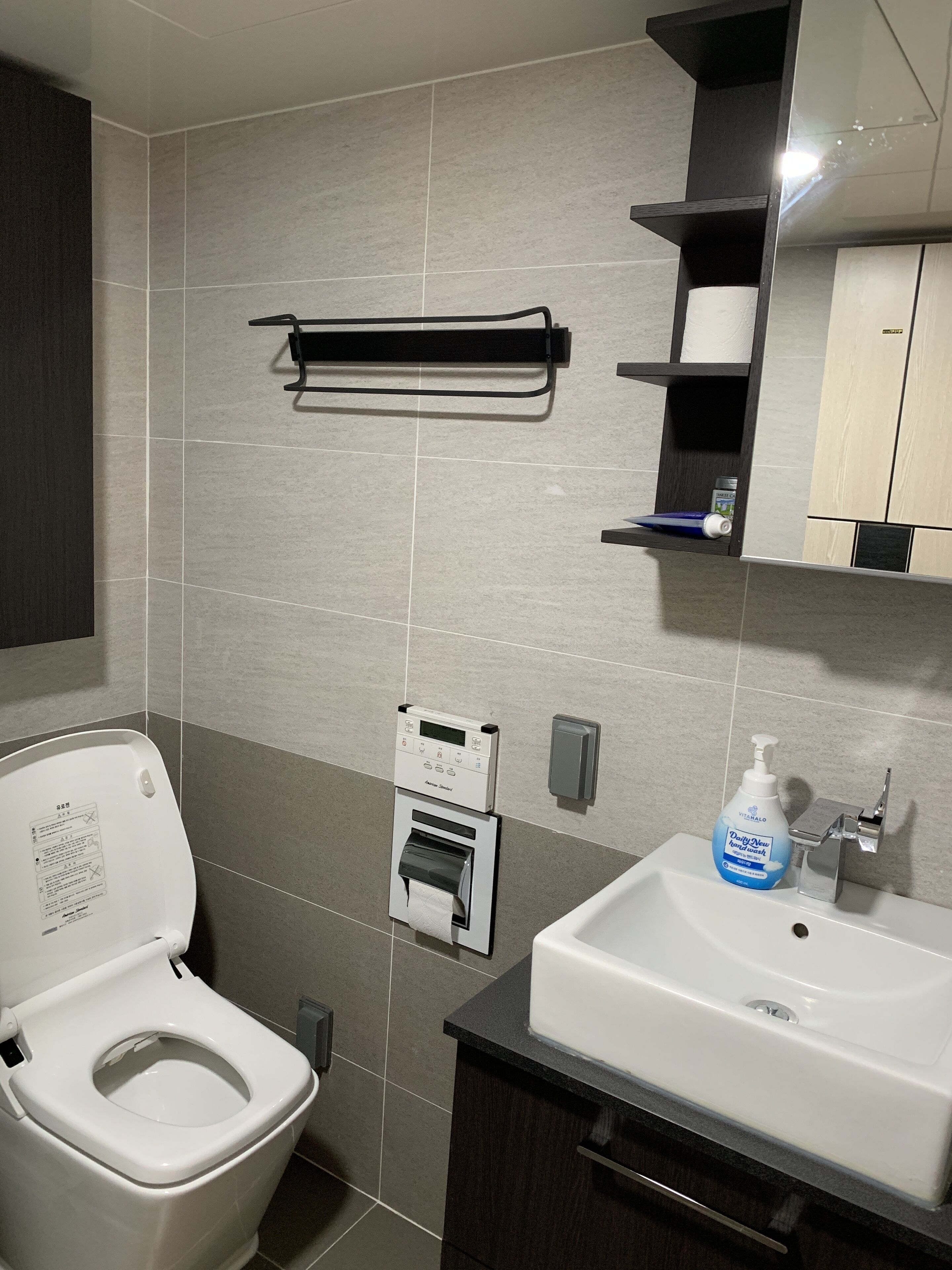 A modern bathroom with a toilet, a sink, a soap dispenser, and a towel rack.