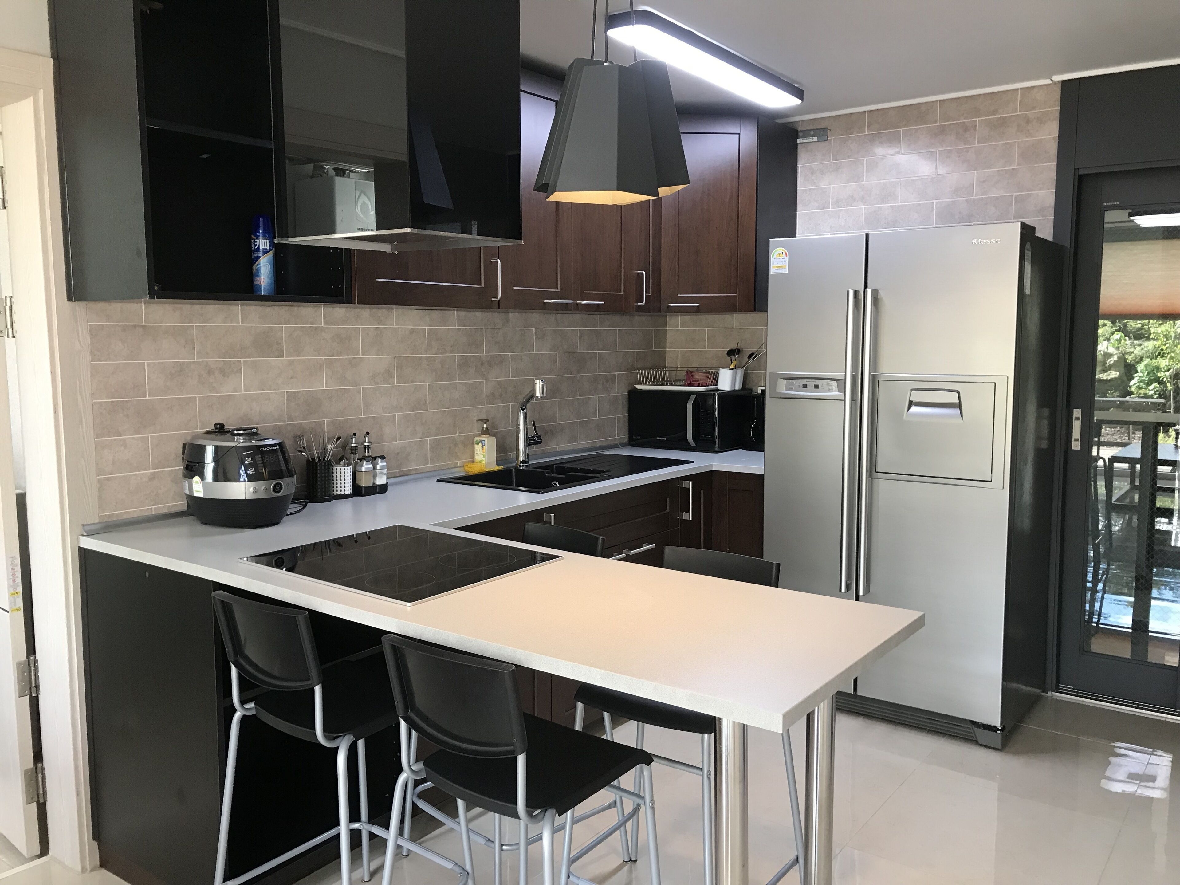 Una cocina moderna con una isla central, taburetes negros, electrodomésticos de acero inoxidable y vistas al exterior.