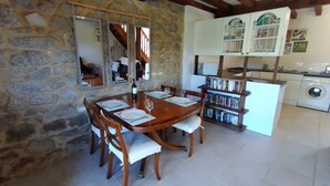 A stone-walled dining area with a wooden table set for four, a bookshelf, and a washing machine in the background. - The Signals - Character cottage, peaceful location, walking distance restaurants (Pluviers)
