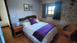 A bedroom with a bed, a nightstand, a chair, and a stone wall. - The Signals - Character cottage, peaceful location, walking distance restaurants (Pluviers)