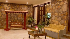 A lobby with a stone wall, a wooden bench, a sofa, and a coffee table. - Vatsalya Vihar - A Luxury Pool Villas Resort (Udaipur)