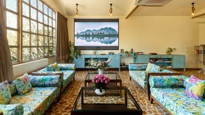 A spacious living room with large windows, a flat-screen TV, and a variety of seating options. - Vatsalya Vihar - A Luxury Pool Villas Resort (Udaipur)