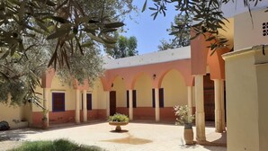 A courtyard with a building featuring arched doorways and columns, surrounded by greenery and potted plants. - Villa Familliale Jardin Piscine (Marrakech)
