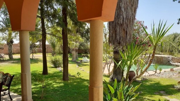A covered outdoor area with a bench, palm trees, and a small pool. - Villa Familliale Jardin Piscine (Marrakech)