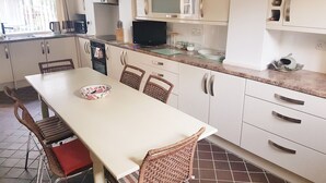 Een kleine keuken met witte kastjes, een eettafel met rieten stoelen en een televisie.