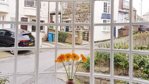 Een erker met een bloemenvaas, een klein beeldje en uitzicht op een straat met huizen en auto's.