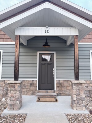 Une maison avec un revêtement extérieur gris, une porte d’entrée marron foncé et des fondations en pierre.