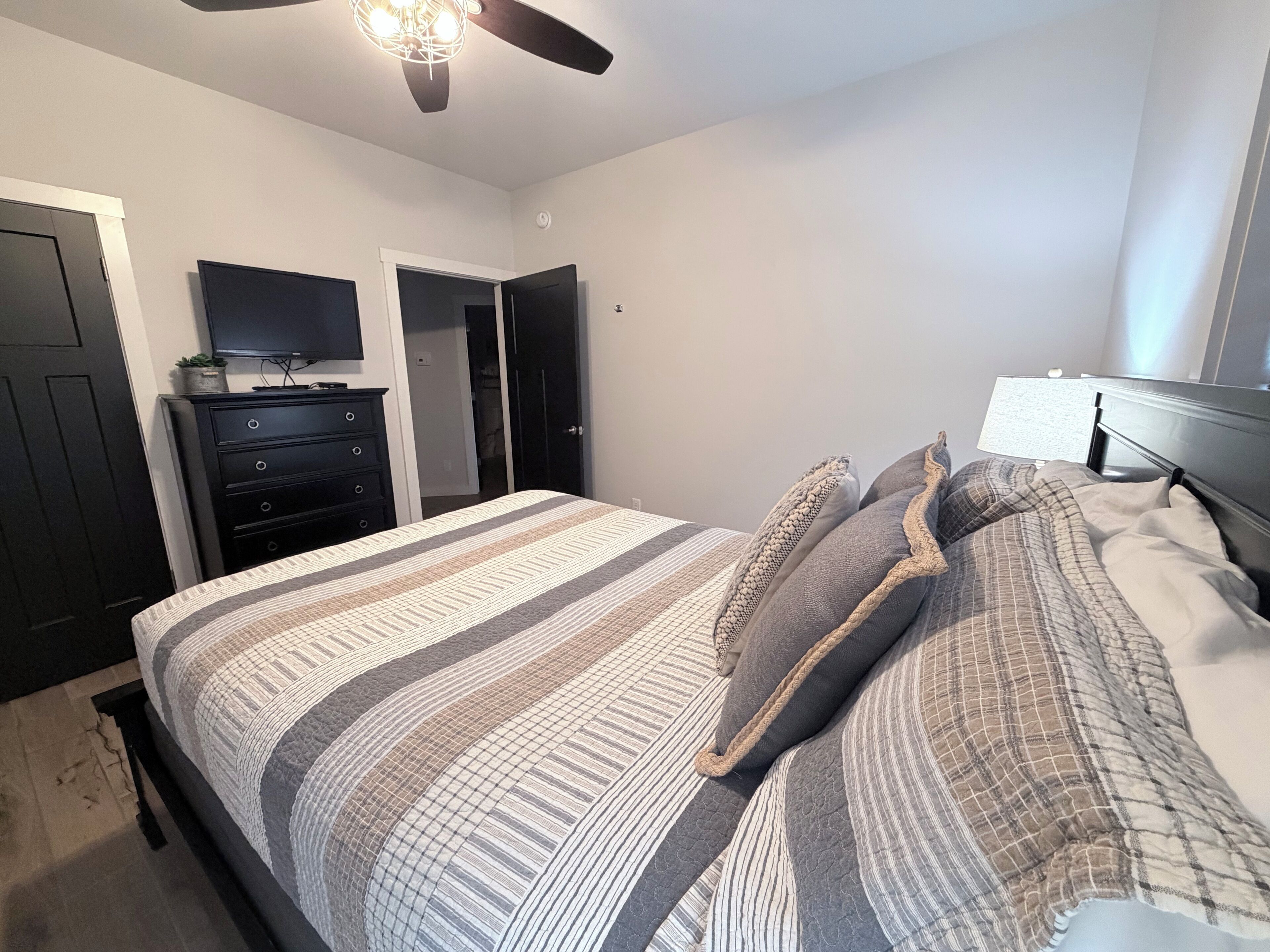 Un dormitorio con una cama, un tocador, un televisor y un ventilador de techo.