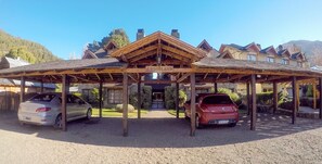 Un área de estacionamiento techada con dos coches, una estructura de madera y un edificio con el rótulo "WOODLAND" al fondo.