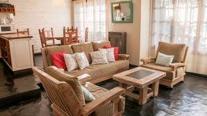Een gezellige woonkamer met een bank, twee fauteuils, een salontafel en een keukenhoek met een magnetron en koffiezetapparaat.