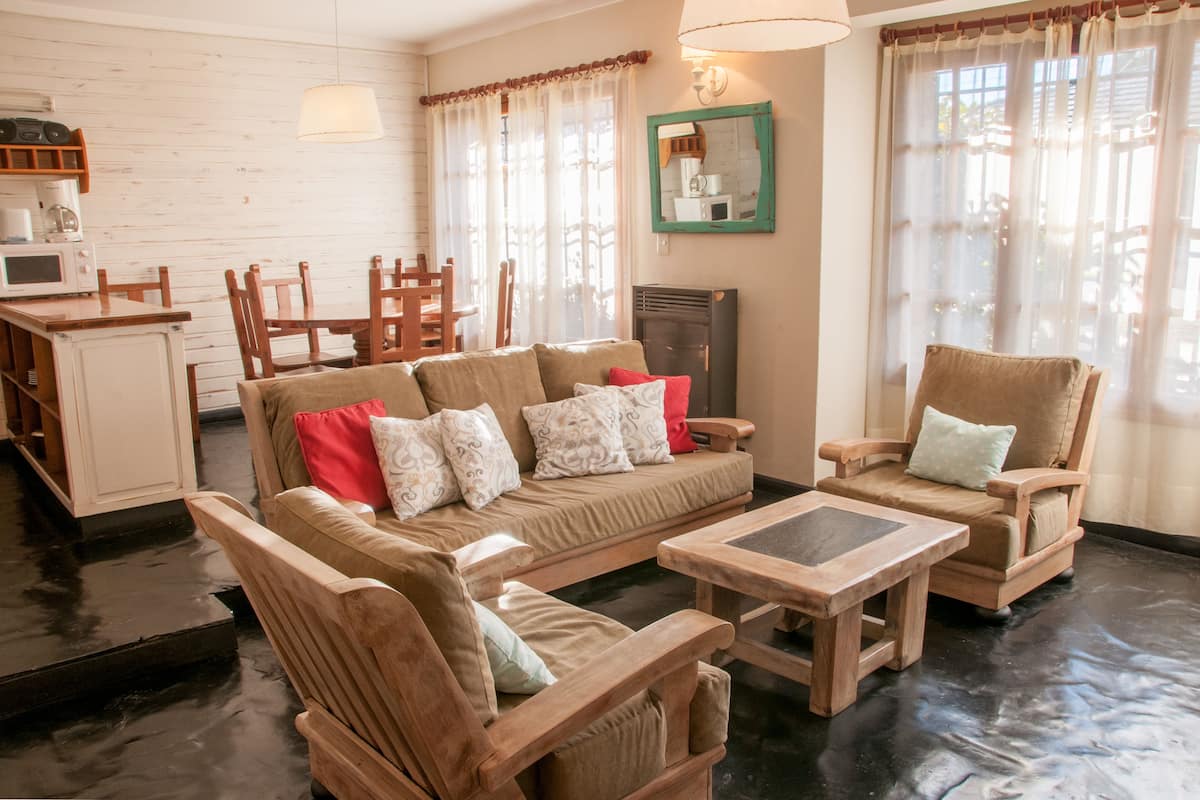 Een gezellige woonkamer met een bank, twee fauteuils, een salontafel en een keukenhoek met een magnetron en koffiezetapparaat.