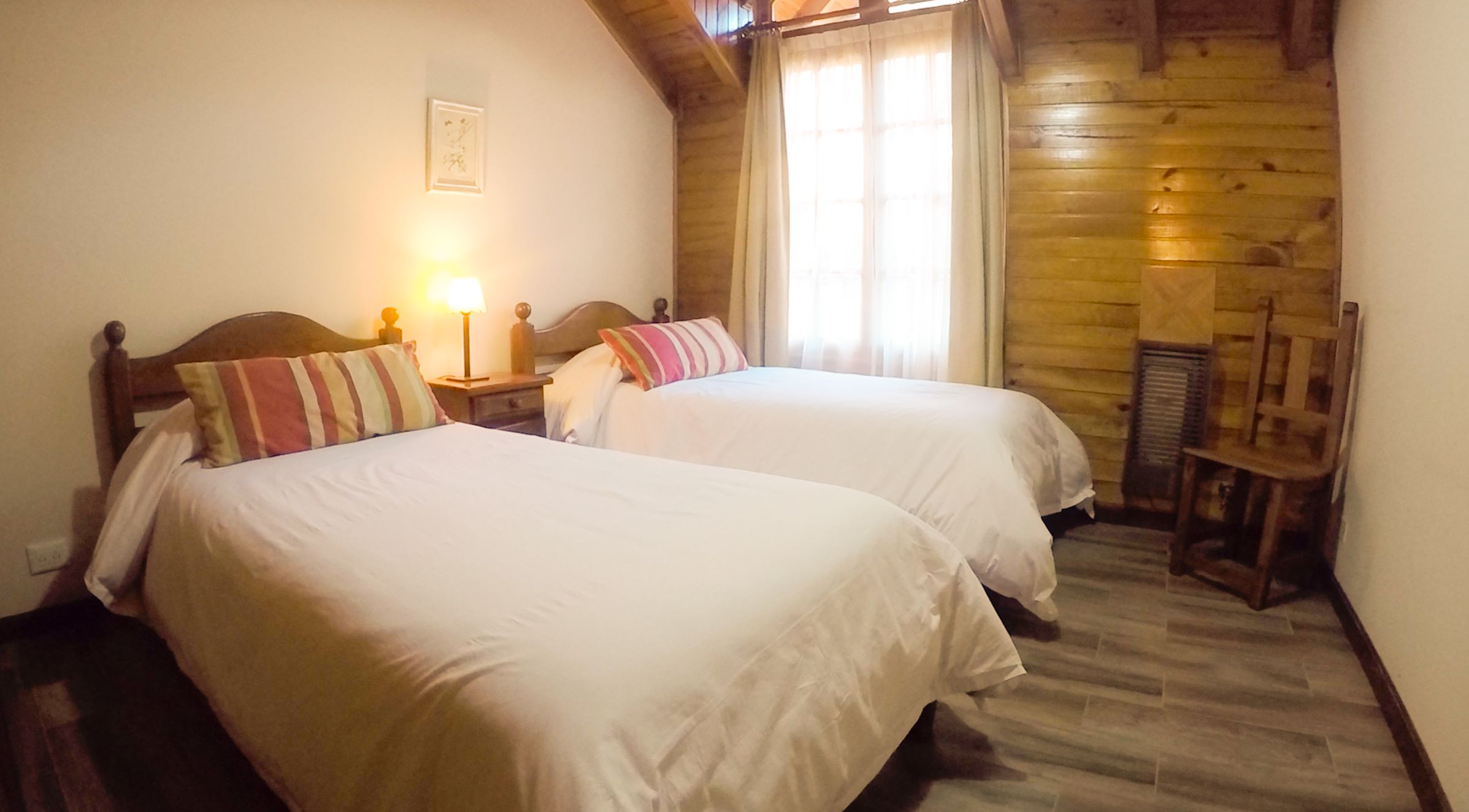 Una habitación con dos camas, techo de madera, ventana con cortinas y un radiador.