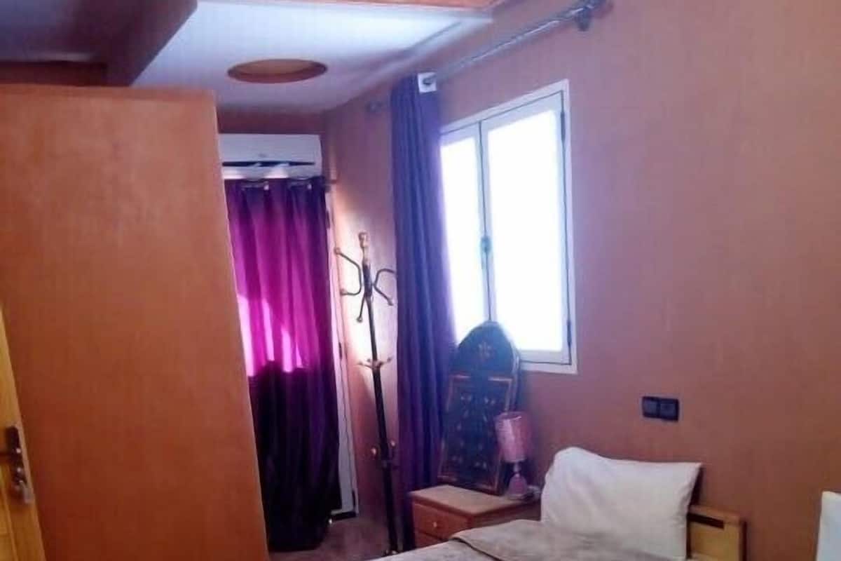 A hotel room with two beds, a window with curtains, a nightstand, and a coat rack.