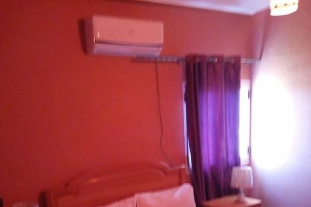A hotel room with a bed, a nightstand, an air conditioning unit, and a window with curtains.