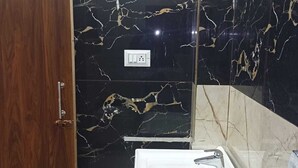 A bathroom with a wooden door, a black marble wall with gold veins, a white sink, and a mirror. - The Century Plaza Hotel (Varanasi)