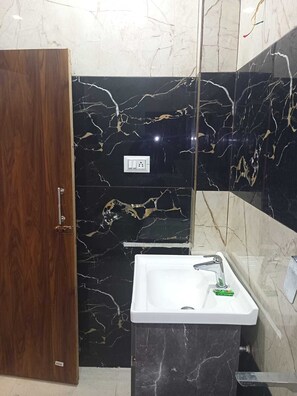A bathroom with a wooden door, a black marble wall with gold veins, a white sink, and a mirror. - The Century Plaza Hotel (Varanasi)