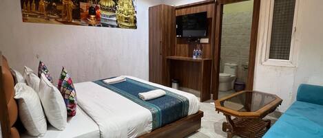 A hotel room with a bed, a sofa, a television, and a minibar.