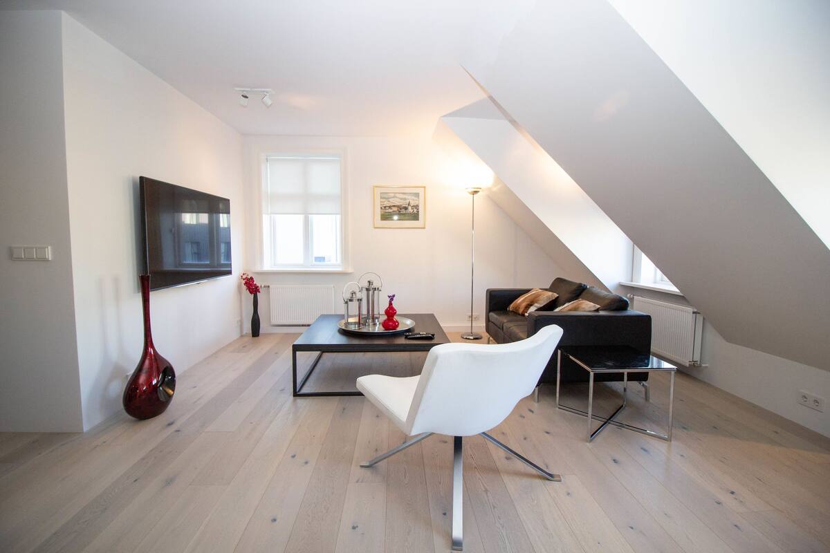 A modern living room with a flat-screen TV, a white chair, a dark sofa, and a coffee table.