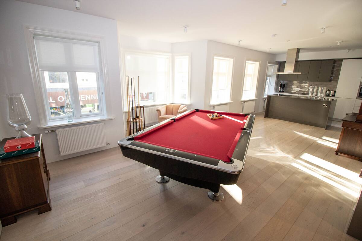 A modern living room with a pool table, a sofa, and a kitchen area.