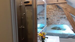 Ein Badezimmer mit Dusche, Waschbecken und Blumenvase, sowie ein Bett vor einer Wand aus Stein und Holzbalken.