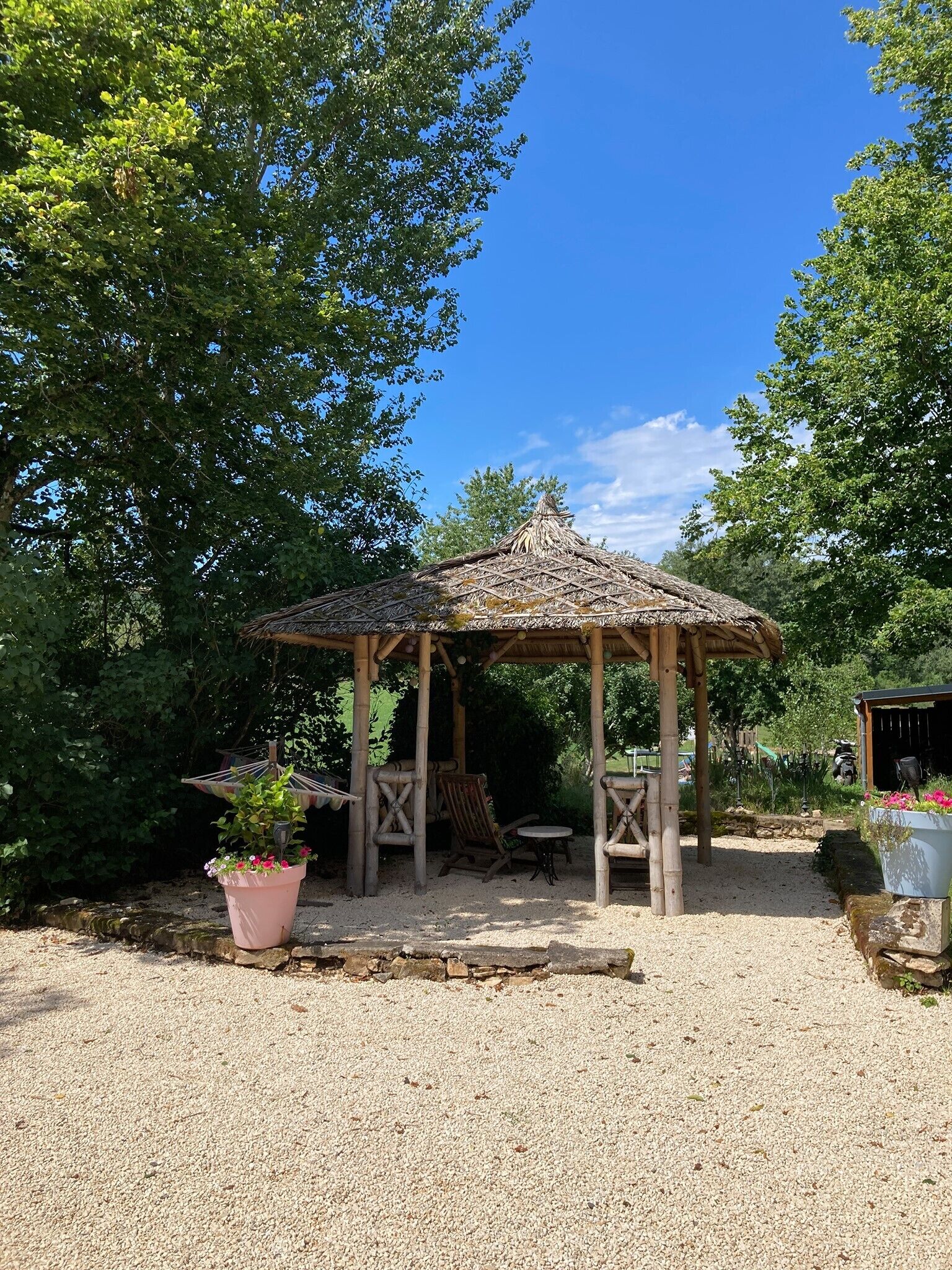 Ein Pavillon aus Holz mit einem Reetdach, umgeben von Kies und Grünpflanzen.