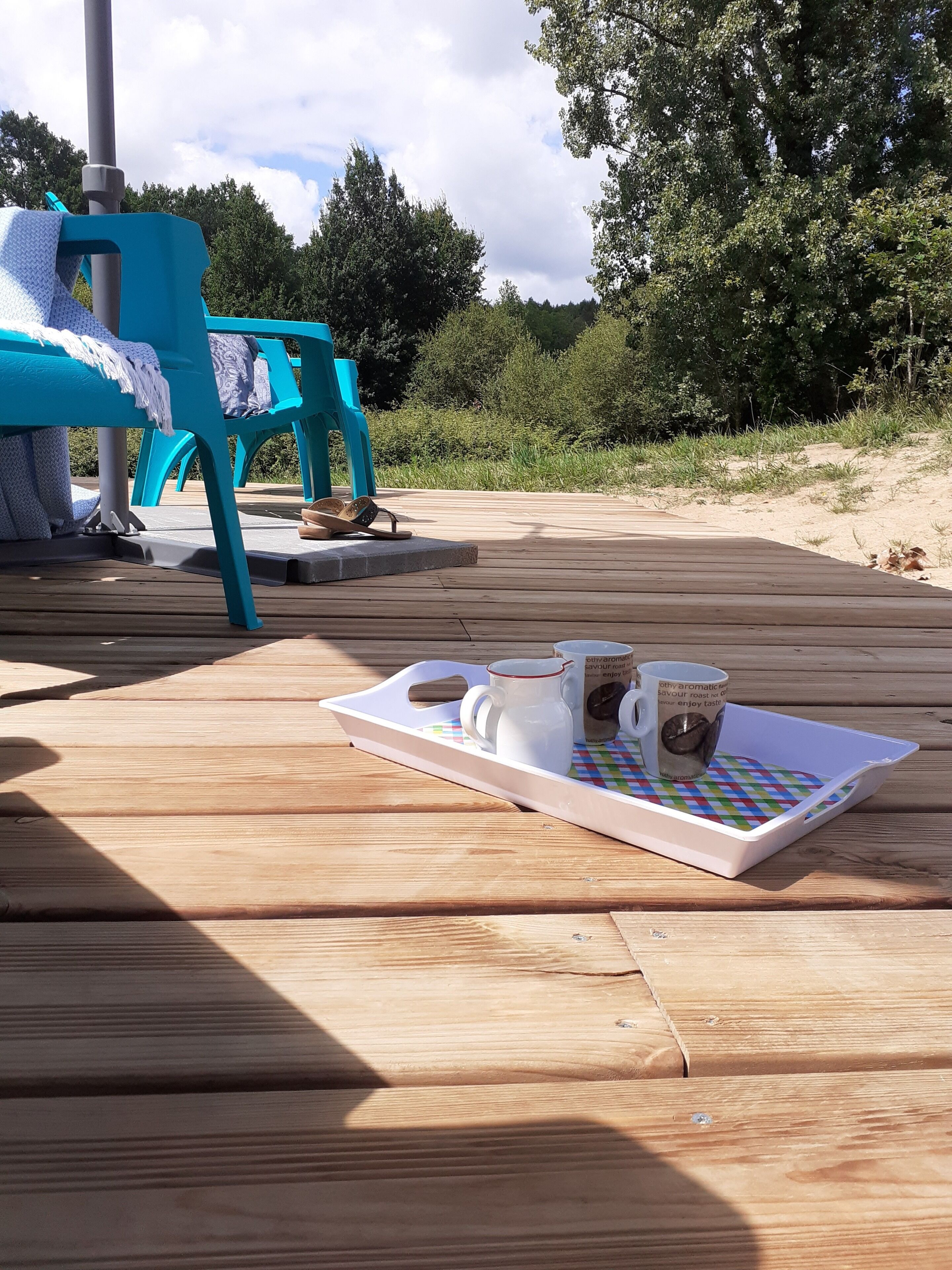 Eine Holzterrasse mit einer Platte voller Speisen und Getränke, einem blauen Stuhl und einem Tisch mit einer Decke.