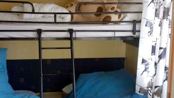 Habitación con literas, un osito de peluche en la litera superior, una colcha azul y una cortina con estampados de animales.