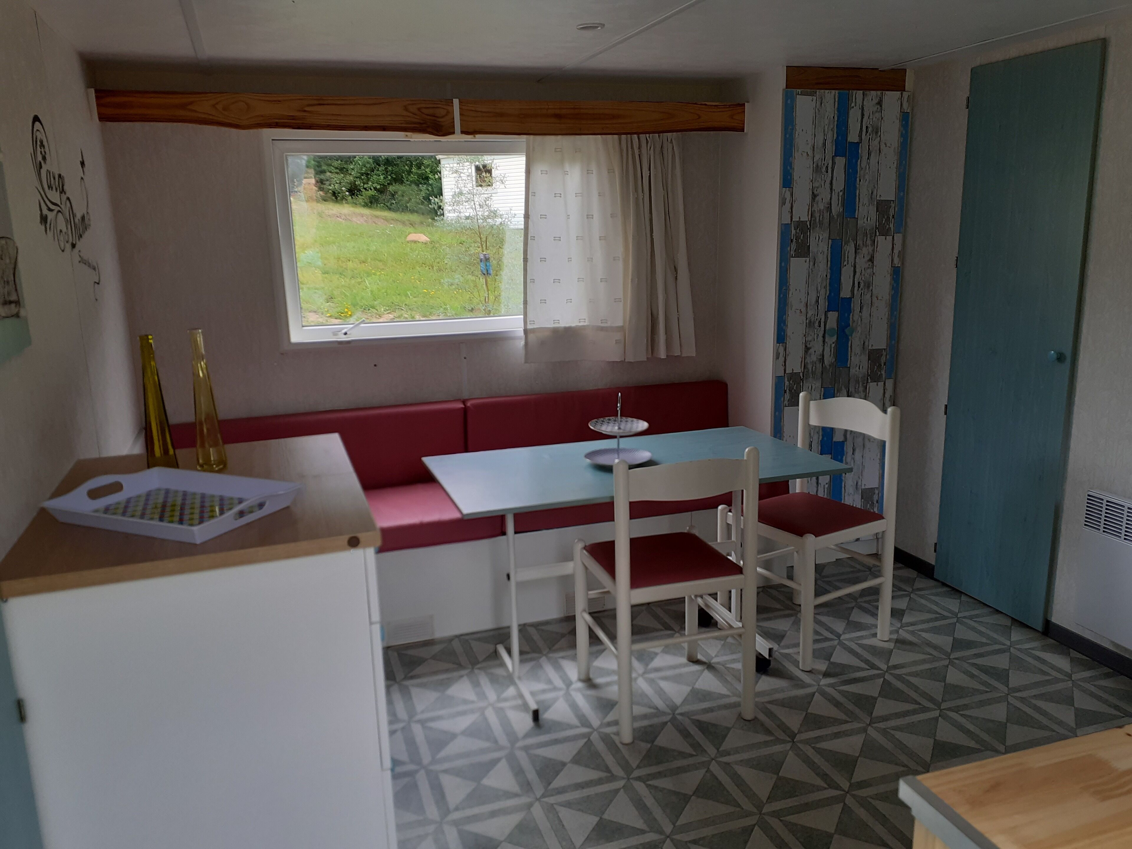 A compact kitchen with a red bench, a table, and a window with curtains.
