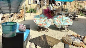 Ein Patio mit Gartenmöbeln, einem Feuerkorb und dekorativen Hängeelementen.