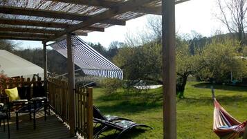 Ein überdachter Außenbereich mit Pergola, einer Hängematte und Blick auf ein Wiesenfeld mit Bäumen.