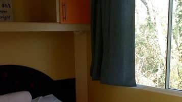 A single-bed room with a headboard, a window with curtains, and a shelf above the bed.
