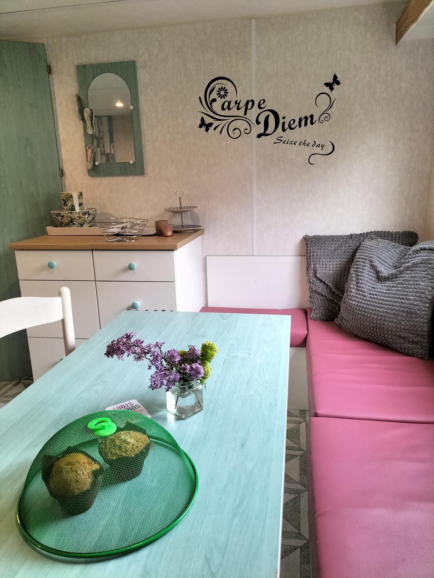 Zona pranzo con tavolo apparecchiato per due, uno specchio sopra il mobile contenitore e un adesivo decorativo a parete.