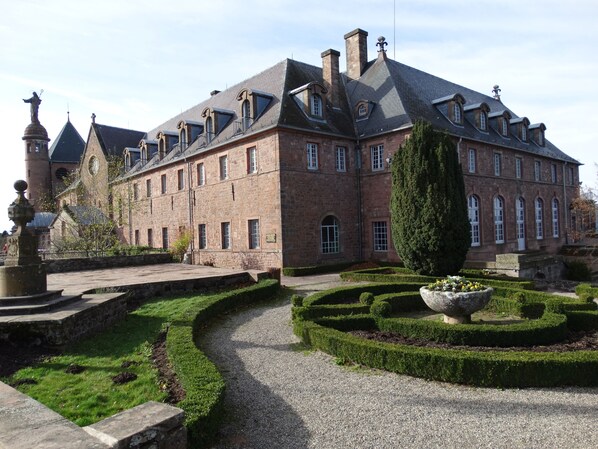 A large, historic building with a symmetrical facade, multiple chimneys, and a central courtyard with a gravel path and neatly trimmed hedges. - HOTELLERIE DU MONT STE-ODILE (Ottrott)