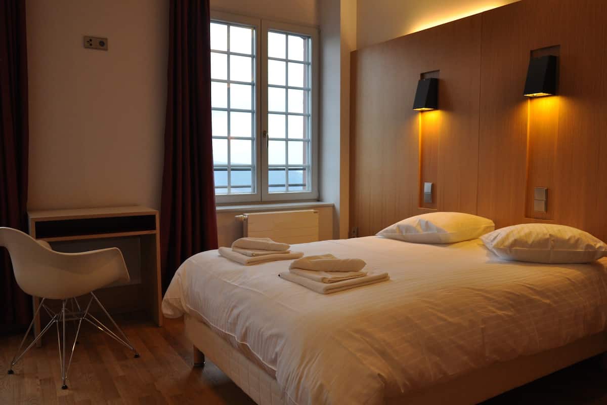Et hotelværelse med seng, skrivebord, stol og et vindue med gardiner.