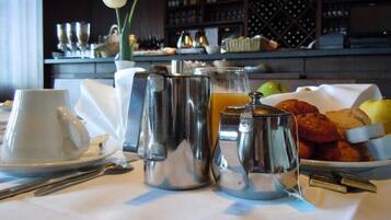 A breakfast setup with a coffee pot, teapot, and cups on a table, accompanied by croissants, apples, and a bowl of fruit.