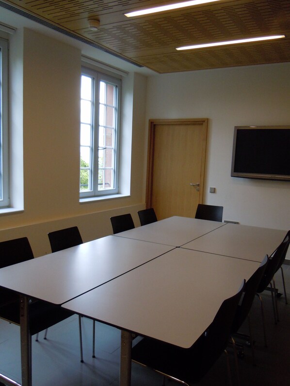 A conference room with a large table, chairs, a door, and a mounted screen. - HOTELLERIE DU MONT STE-ODILE (Ottrott)