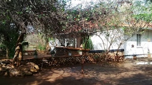 Un muro de piedra rústico con una terraza de madera, rodeado de abundante follaje y un edificio blanco con ventanas.